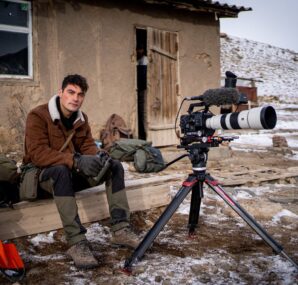 Dan with a camera next to large wall of rocks