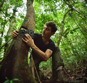 Dan with a camera next to large wall of rocks