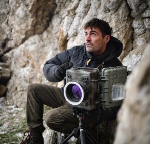 Dan with a camera next to large wall of rocks