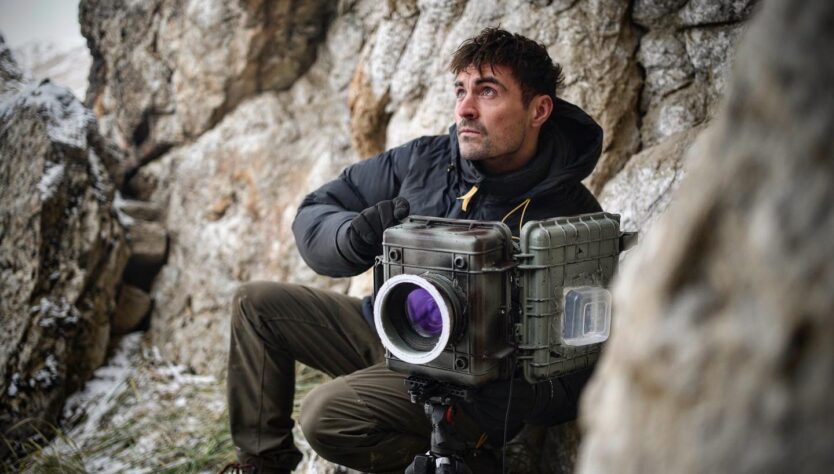 Dan with a camera next to large wall of rocks