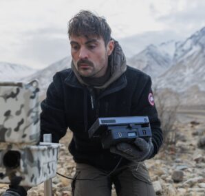 Dan with a camera next to large wall of rocks