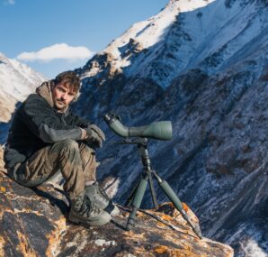 Dan with a camera next to large wall of rocks