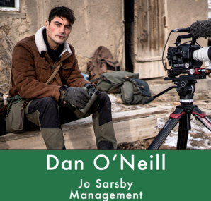 Dan with a camera next to large wall of rocks